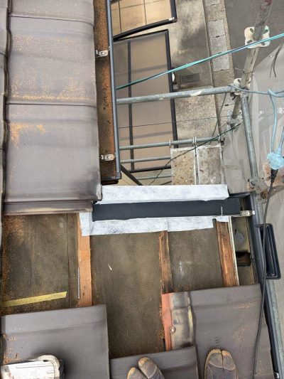 屋根のケラバ（袖瓦）補修工事において、侵入した雨水を雨樋へ安全に排水するための金属製ケラバ水切り板金が下地の上に設置されている様子