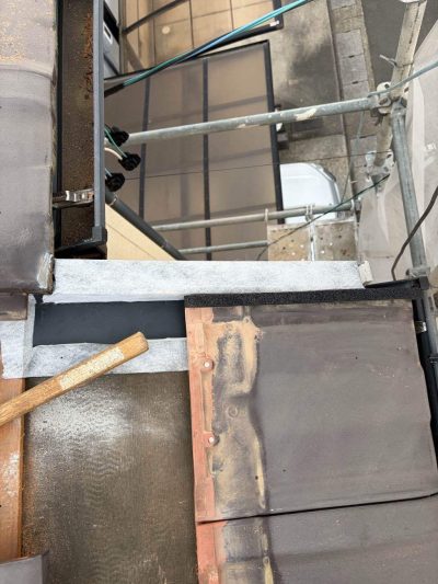 ケラバ水切りの上に黒い防水シーラーを貼り、その上からブラウン色の平瓦を丁寧に納めていく屋根修理の様子