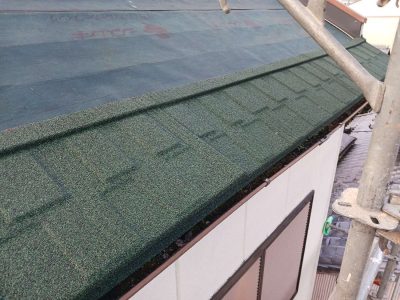 岐阜市H様邸の屋根カバー工法施工中。防水シートが敷かれた屋根の軒先側から、天然石付き軽量金属屋根「Tルーフ（グリーン）」を1段目から順に葺き進めている様子