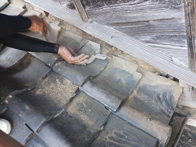 下屋の流れ部分で瓦の下にある既存の土を撤去する職人